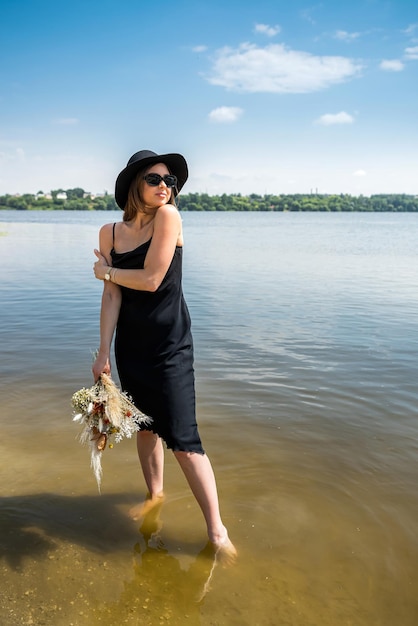 Hübsche Frau, die barfuß im schwarzen Abendkleid im Stadtsee spazieren geht