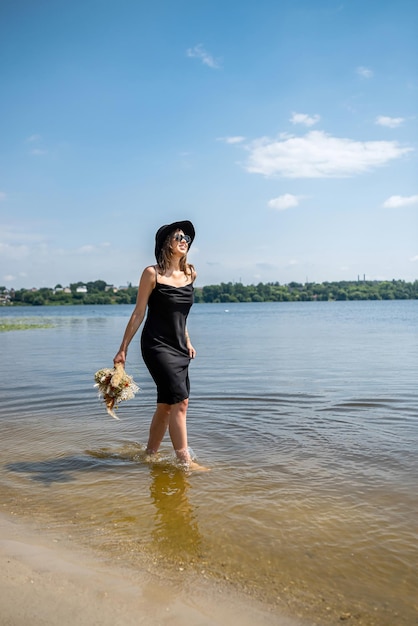 Hübsche Frau, die barfuß im schwarzen Abendkleid im Stadtsee spazieren geht