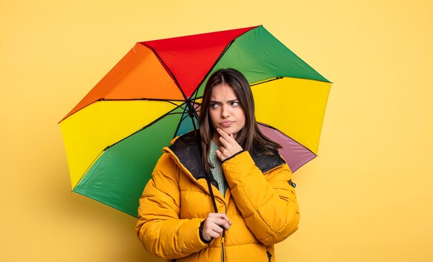 Hübsche Frau, die denkt, sich zweifelhaft und verwirrt fühlt. Winter- und Regenschirmkonzept