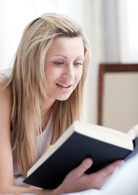 Hübsche Frau, die ein Buch liegt auf ihrem Bett liest