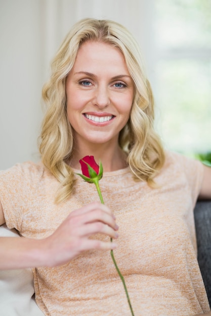 Hübsche Frau, die eine Rose im Wohnzimmer riecht