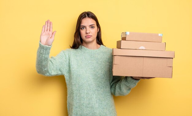 Foto hübsche frau, die ernst aussieht und offene handfläche zeigt, die das konzept der stop-gesten-pakete-boxen macht