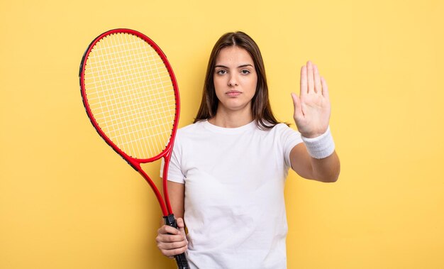 Hübsche Frau, die ernst aussieht und offene Handfläche zeigt, die Stoppgeste macht. Tennisspieler-Konzept