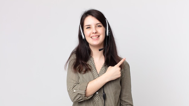 Hübsche Frau, die fröhlich lächelt, sich glücklich fühlt und auf die Seite zeigt. Assistant Agent mit Headset