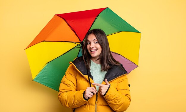 Hübsche Frau, die fröhlich lächelt, sich glücklich fühlt und auf die Seite zeigt. Winter- und Regenschirmkonzept