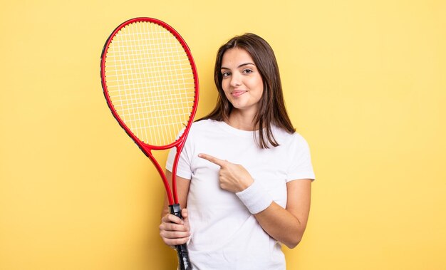 Hübsche Frau, die fröhlich lächelt, sich glücklich fühlt und zur Seite zeigt. Tennisspieler-Konzept