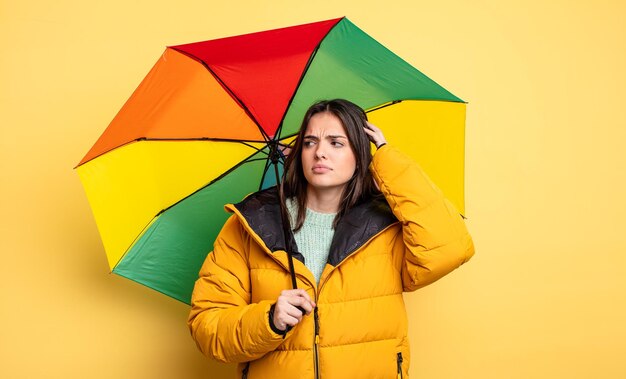 Hübsche Frau, die glücklich lächelt und tagträumt oder an Winter- und Regenschirmkonzept zweifelt