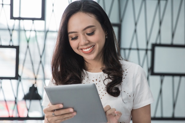 Hübsche Frau, die lächelt, während sie Tablette benutzt