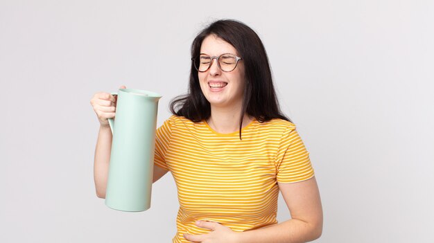 Hübsche Frau, die laut über einen lustigen Witz lacht und eine Kaffee-Thermoskanne hält