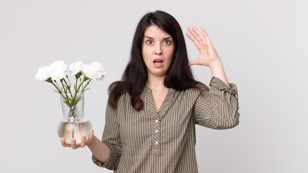 Hübsche Frau, die mit den Händen in die Luft schreit und dekorative Blumen hält. Assistant Agent mit Headset