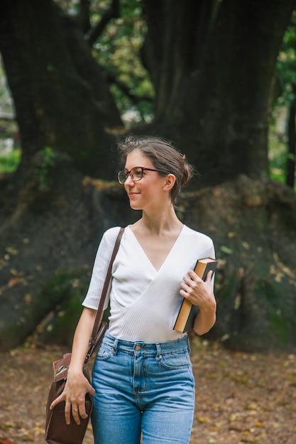 Hübsche Frau, die mit Literatur durch den Park geht