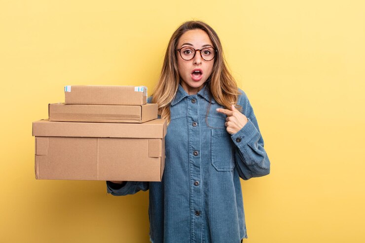 Foto hübsche frau, die schockiert und überrascht mit weit geöffnetem mund aussieht und auf sich selbst zeigt. paketboxen-konzept