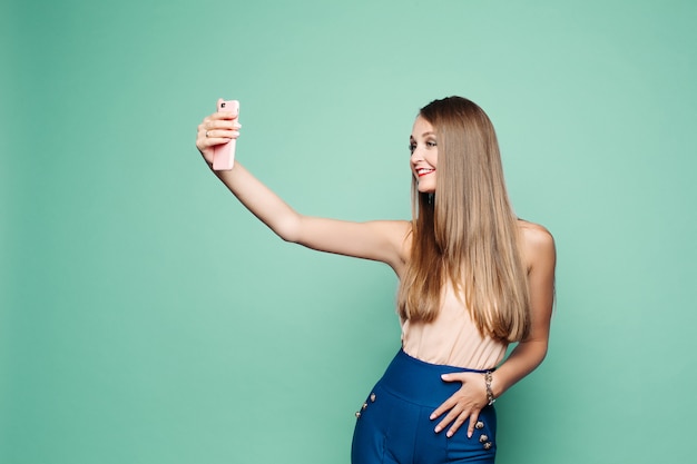 Hübsche Frau, die selfie über Handy über grünem Hintergrund nimmt.