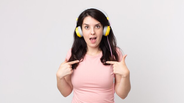 Hübsche Frau, die sich glücklich fühlt und mit einer aufgeregten Musik mit Kopfhörern auf sich selbst zeigt