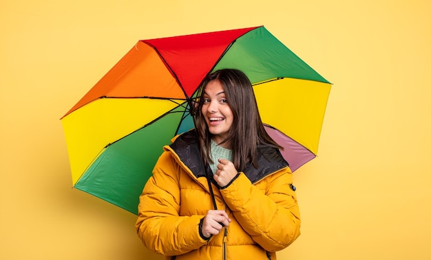 Hübsche Frau, die sich glücklich fühlt und vor einer Herausforderung steht oder feiert. winter- und regenschirmkonzept