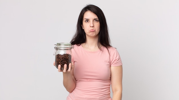 Hübsche Frau, die sich traurig und weinerlich mit einem unglücklichen Blick fühlt und weint und eine Kaffeebohnenflasche hält