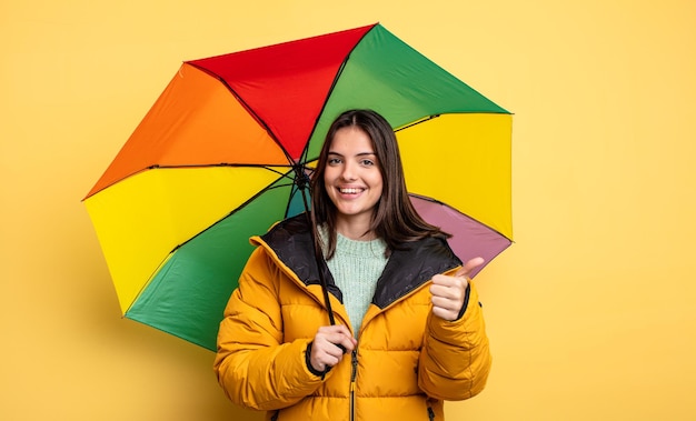 Hübsche Frau, die stolz ist und positiv mit Daumen nach oben lächelt. Winter- und Regenschirmkonzept