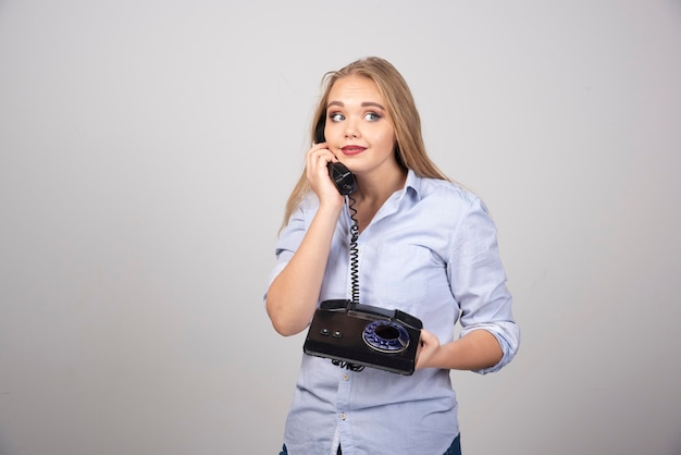 hübsche frau, die telefon hält und isolierte graue wand spricht.