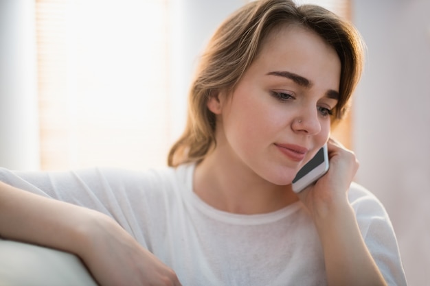 Hübsche Frau, die um das Telefon auf der Couch im Wohnzimmer ersucht