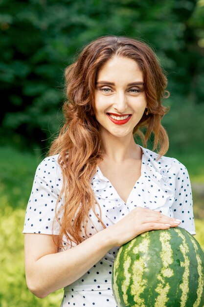 Hübsche Frau hält eine ganze Wassermelone im Freien.