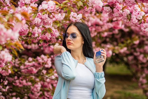 Hübsche Frau hält Parfüm. Duftwasser Köln in Sprühflasche. Duft liegt in der Luft nach Ihnen. Mädchen riechen Tester. sexy Frau halten Parfümflasche. Parfümflasche, die Blumen sprüht.