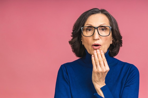 Hübsche Frau im Alter, die sich schockiert und aufgeregt fühlt, lacht, erstaunt und glücklich ist, weil eine unerwartete Überraschung auf rosafarbenem Hintergrund isoliert ist.