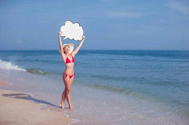 Hübsche Frau im Bikini mit Blasensprache in den Händen am Strand