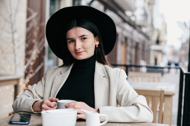 Foto hübsche frau im schwarzen fedora-hipster-hut, der kaffee in einem café genießt