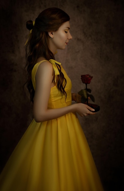 Hübsche Frau in der gelben Kleidnahaufnahme mit roter Rose in ihren HändenBeauty und das Biest Cosplay