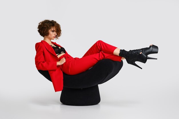 Hübsche Frau in roten Pantsui und Pole Dance Stiefeln sitzt in einem weichen Sessel im Profil
