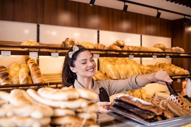 Hübsche Frau in Schürze, die frisch gebackenes süßes Gebäck und Brot in der Bäckerei verkauft