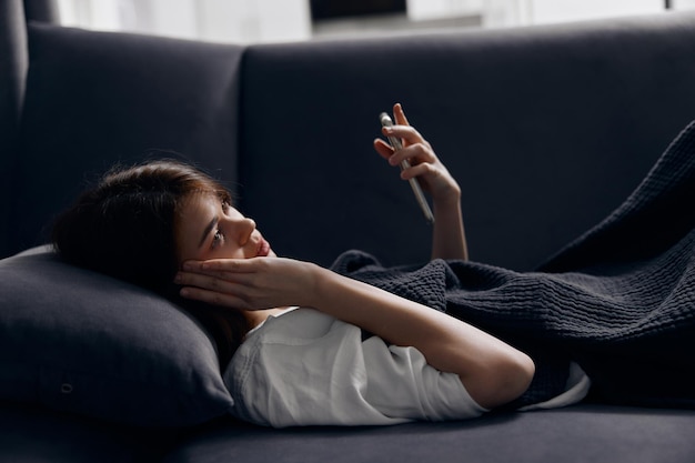 Hübsche Frau liegt auf dem Sofa und hat einen ausgeschnittenen Blick auf ihr Mobiltelefon