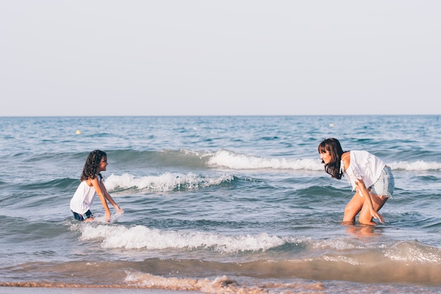 Hübsche Frau mit der kurzen Blue Jeans und ihrer Tochter, die im Strand spielen, wässern