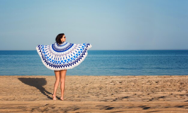 Hübsche Frau mit einem runden Strandteppich des Mandalas in der Ozeanküste