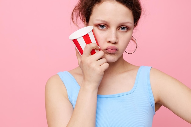 Hübsche Frau mit Einwegglas, die Emotionen aufwirft, rosa Hintergrund unverändert