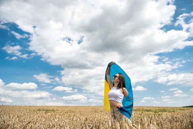 Hübsche Frau mit gelb-blauer Flagge der Ukraine im Weizenfeld