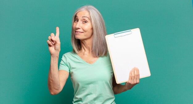 Hübsche Frau mit grauem Haar, die ein leeres Blatt Papier zeigt