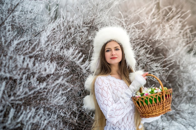 Hübsche Frau mit Körben und weißem Pullover, Pelzmütze im Winterschneepark