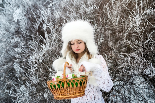 Hübsche Frau mit Körben und weißer Pelzmütze im Winterschneepark