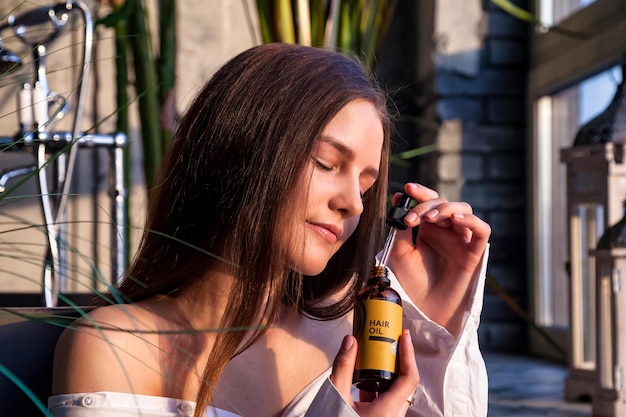 Hübsche Frau mit Pipette und Kosmetik-HAARÖL-Flasche zum Auftragen von Tropfen auf Haut oder Haar