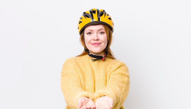 Hübsche Frau mit rotem Kopf, die glücklich mit freundlichen Lächeln lächelt und ein Konzeptradfahrkonzept anbietet und zeigt