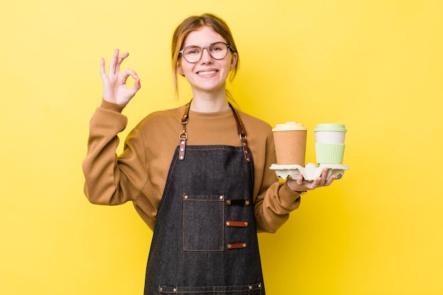 Hübsche Frau mit rotem Kopf, die sich glücklich fühlt und die Zustimmung mit der Geste "OK" zum Mitnehmen des Kaffeekonzepts zeigt