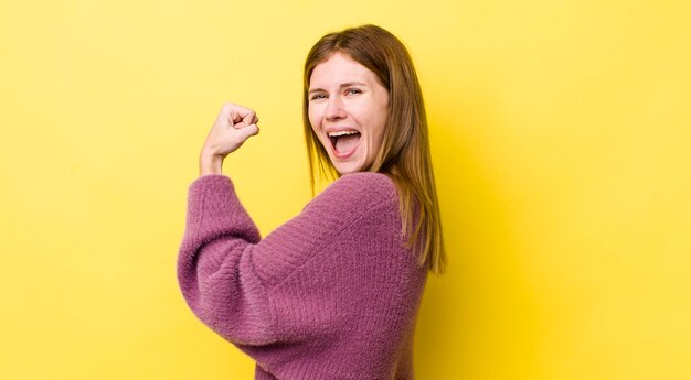 Hübsche Frau mit rotem Kopf, die sich glücklich fühlt, zufrieden und kraftvoll, fit und muskulöser Bizeps, der nach dem Fitnessstudio stark aussieht