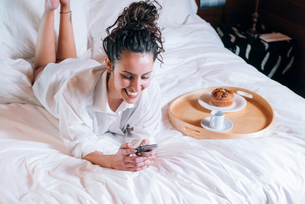 Hübsche Frau mit Telefon im Bett