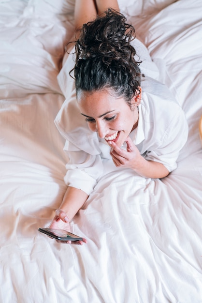 Hübsche Frau mit Telefon im Bett