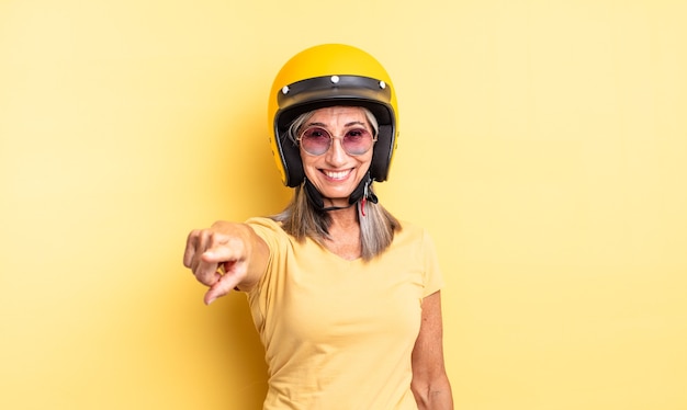 hübsche frau mittleren alters, die auf die kamera zeigt, die dich auswählt. Motorradhelmkonzept