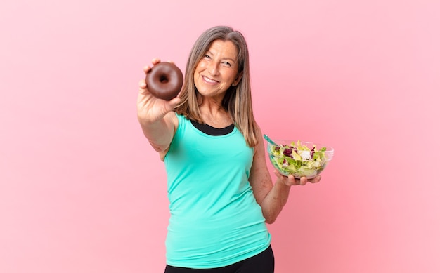 Hübsche Frau mittleren Alters, die einen Salat und einen Donut verarbeitet