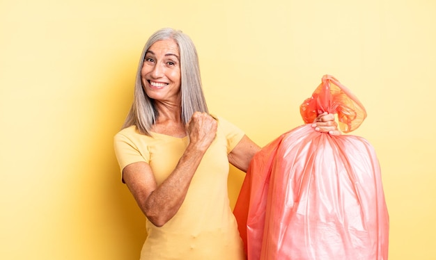 Hübsche Frau mittleren Alters, die sich glücklich fühlt und einer Herausforderung gegenübersteht oder feiert. Müllbeutel aus Plastik