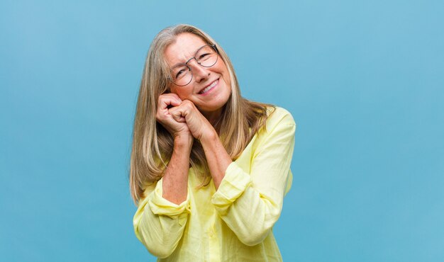 Hübsche Frau mittleren Alters, die sich glücklich und verliebt fühlt und mit einer Hand neben dem Herzen und der anderen vorne gestreckt lächelt