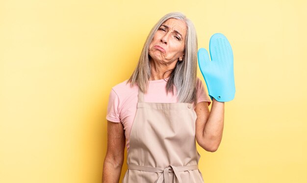 Hübsche Frau mittleren Alters, die sich traurig und weinerlich fühlt, mit einem unglücklichen Blick und einem weinenden Ofenhandschuh-Konzept